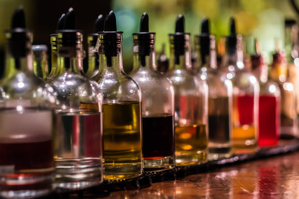 Glass syrup bottles with pour spouts lined up on a bar counter.