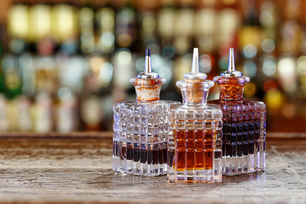 Three cut-glass dasher bottles with pour spouts on a wooden bar counter.