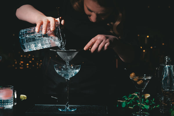 Drink poured from a mixing glass through a Hawthorne strainer and a fine-mesh sieve into a coupe.