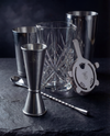The Full Bar: Boston Shaker, Crystal Mixing Glass, Hawthorne Strainer, Jigger, and Bar Spoon on a dark slate surface.