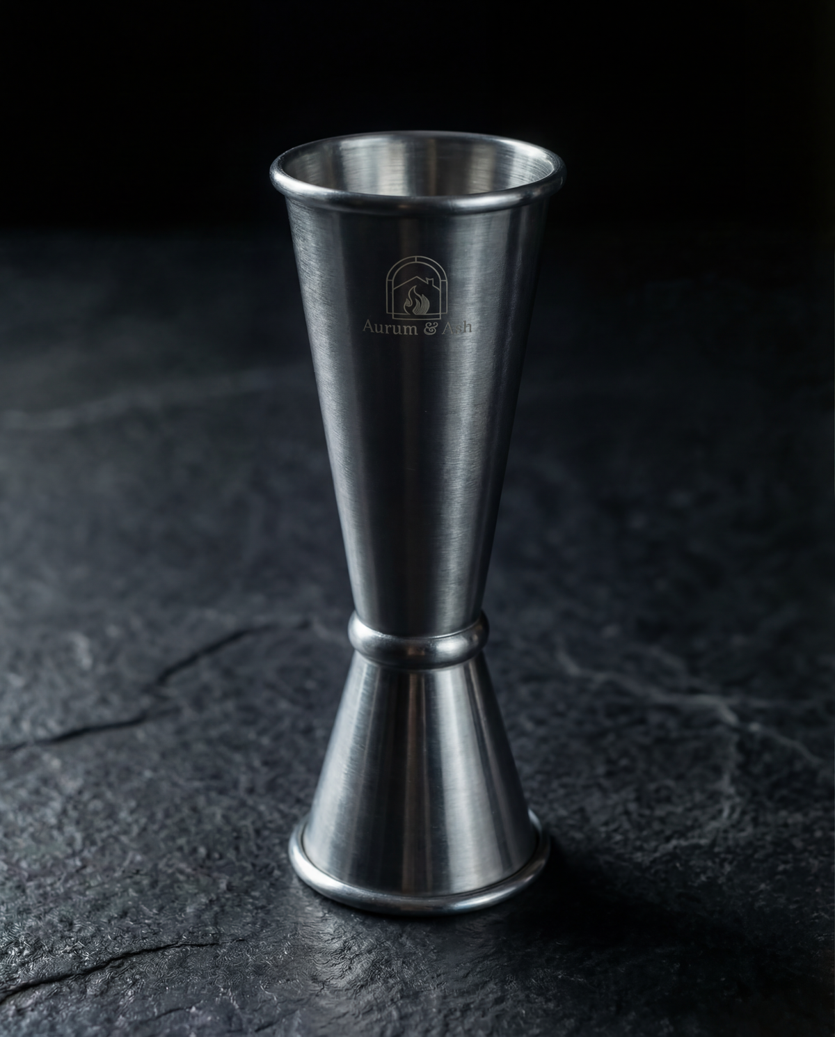 Double-sided stainless steel Jigger standing upright, Aurum & Ash logo etched on the side.
