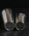 Both tins of the Boston Shaker on their sides, Aurum & Ash logo etched on each base.